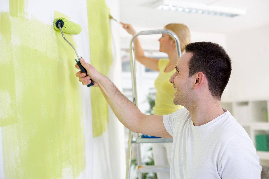 Young smiling couple painting home with yellow color 