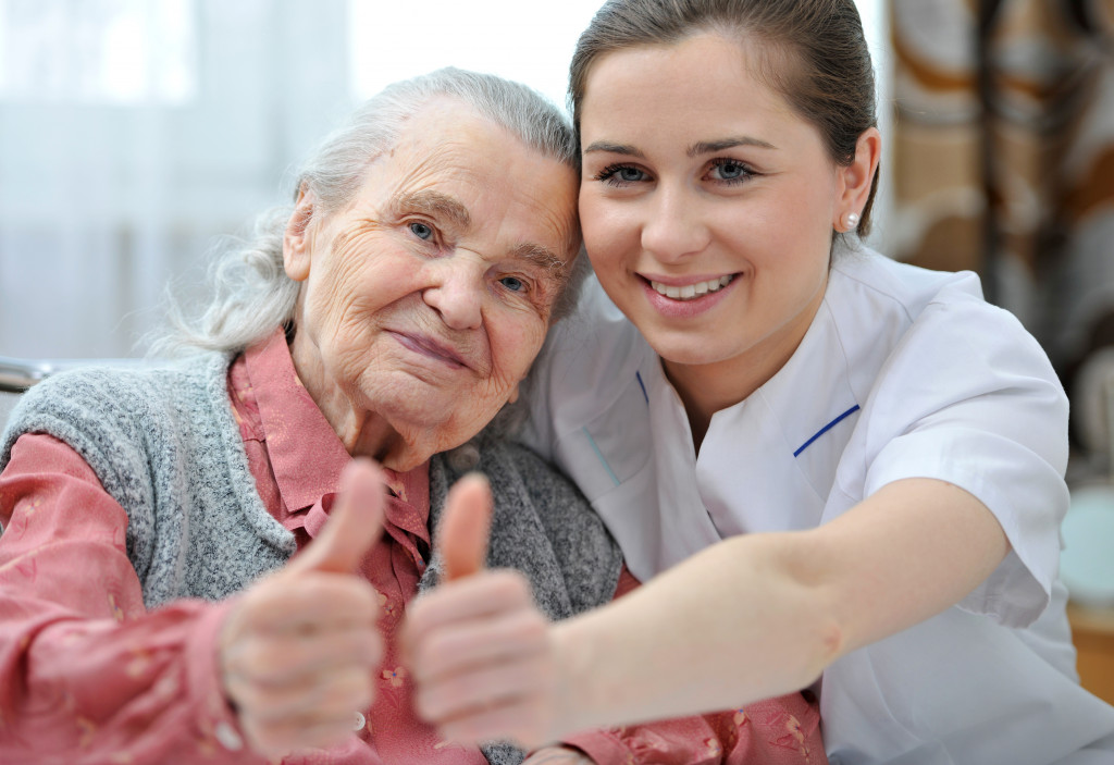 an older woman and a younger female caregiver sitting side by side and doing a thumbs up