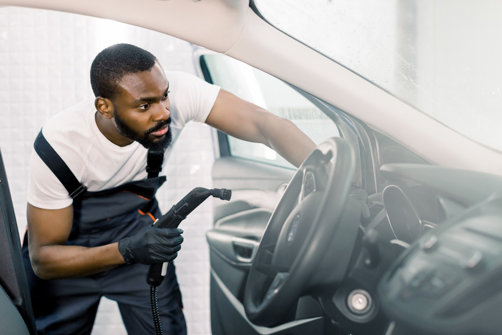 a young man using a steamer to clean a car dashboard