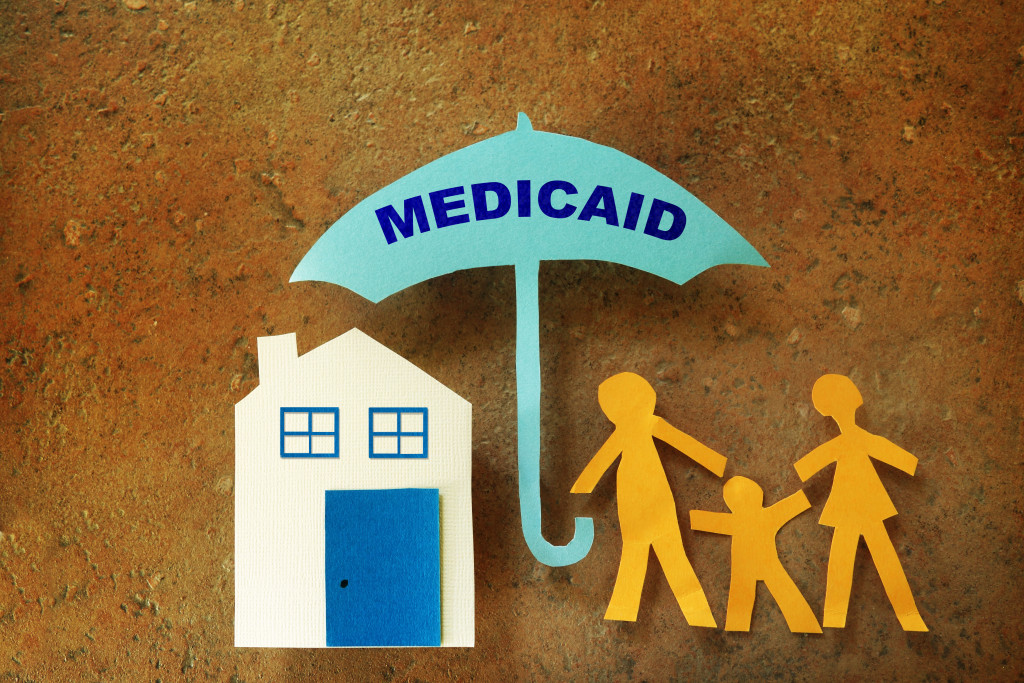 A paper art of family standing under medicaid umbrella with house