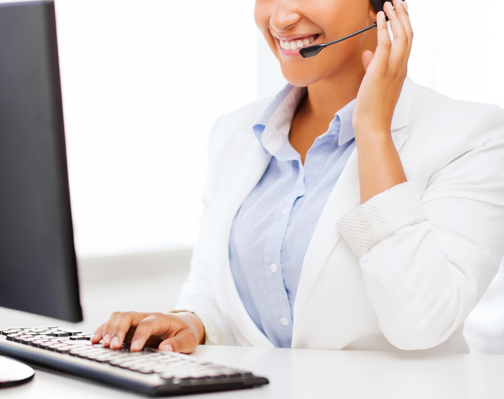 A woman wearing a headphone with a microphone using a computer at a reception desk