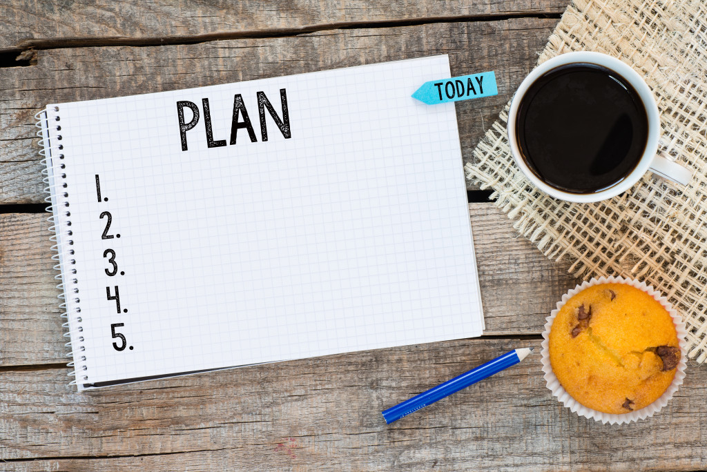 Notebook with an action plan and sticker today on wooden desk with cup of coffee and muffin