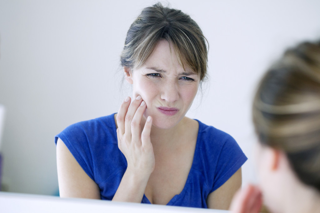 Young woman looking in mirror and holding her jaw in pain