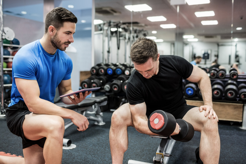 A handsome and fit trainer watching a handsome and fit client doing bicep curls in the gym