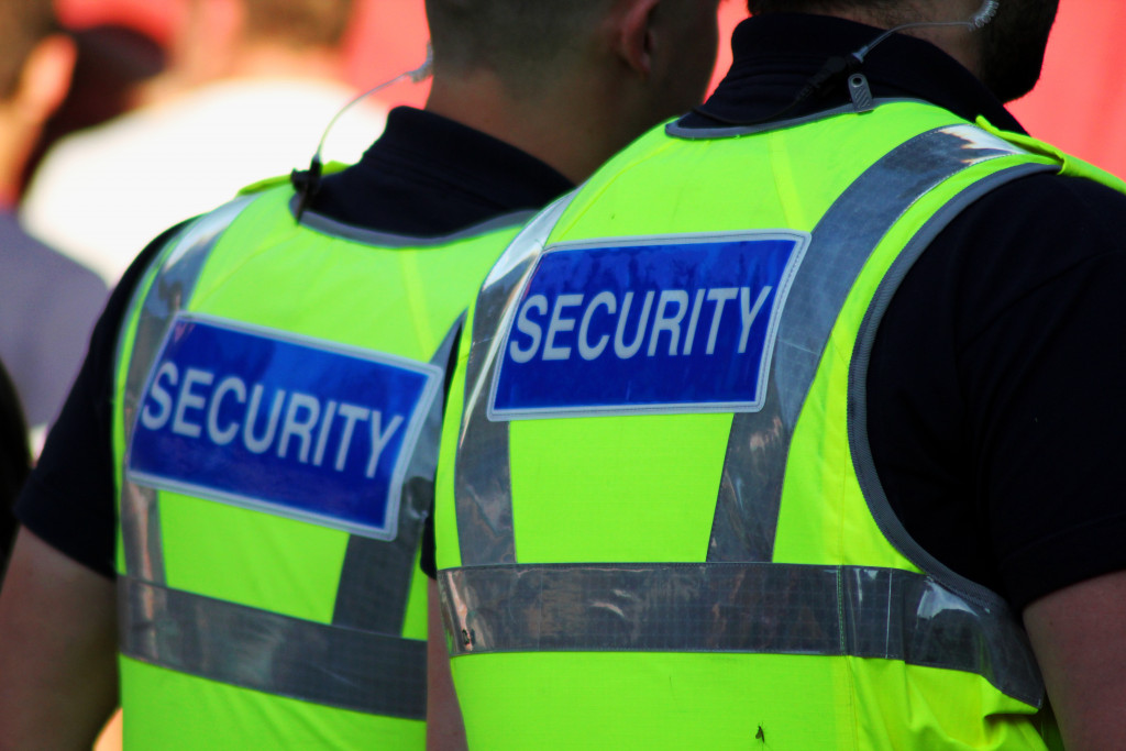 Two male security guards wearing bright tops on with the word 'security' at their backs