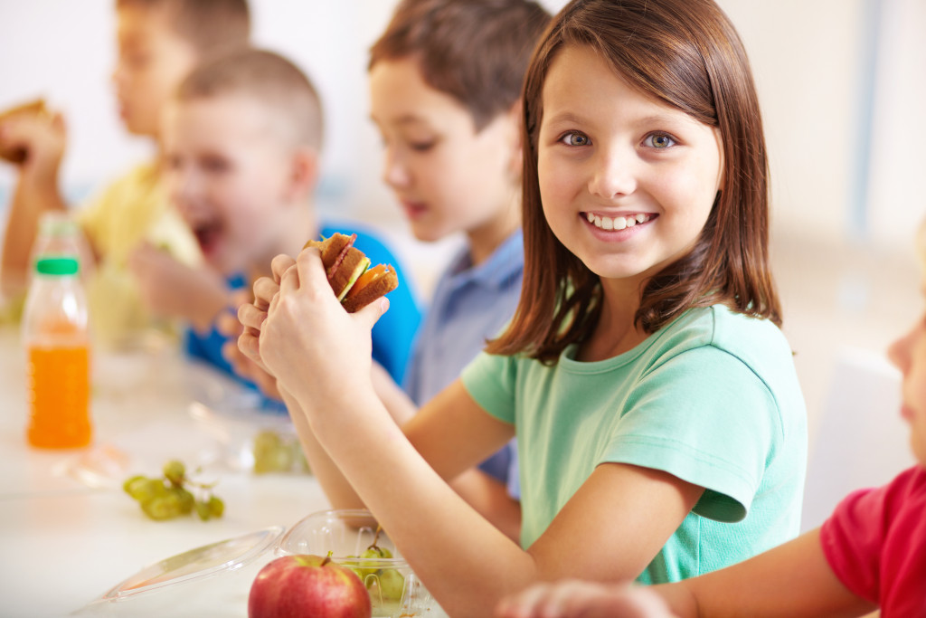 A child eating a sandwich on a table with fruits