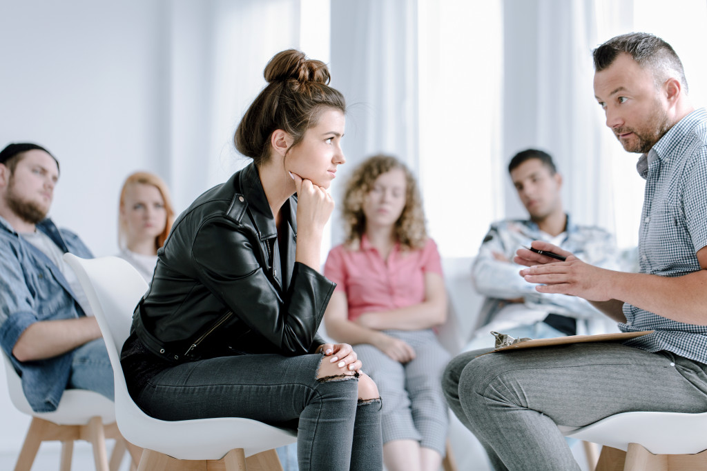 Rebellious young girl listening to her counselor during appointment with problematic teenagers