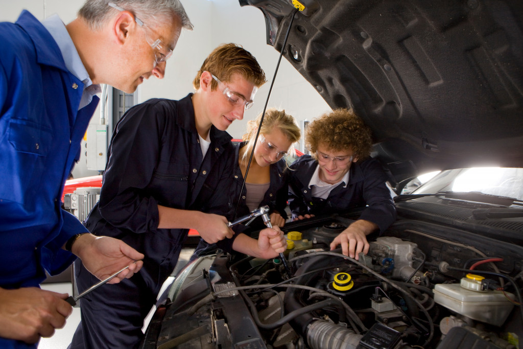 elderly man teaching teenagers how to fix a car's engine
