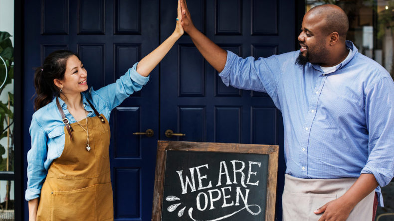 Cheerful business owners standing with open blackboard