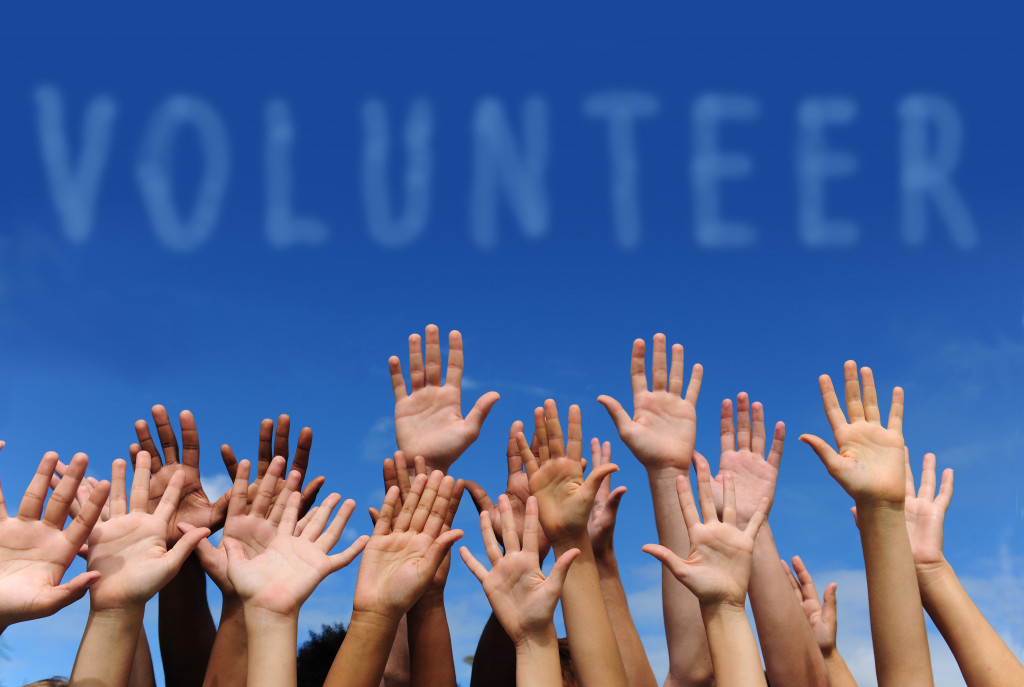 multiple hands raised in the air with word volunteer in the blue sky as background