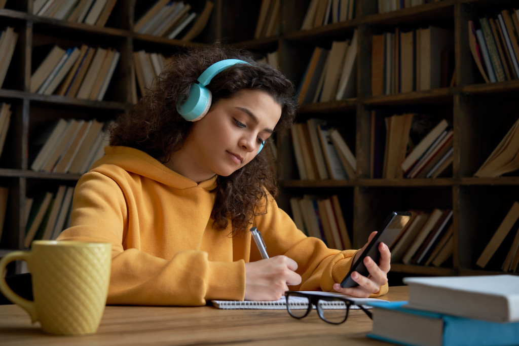 a young girl holding a phone taking notes while listening on a headphone