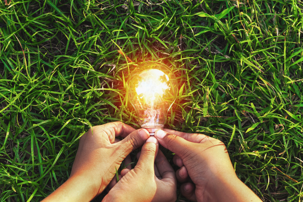 Three hands holding a lit light bulb on the grass