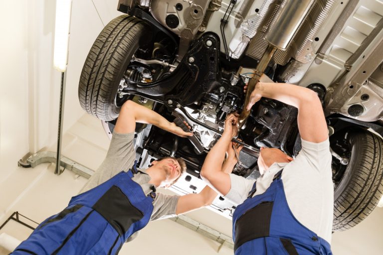 Two mechanics working on the underside of a vehicle.